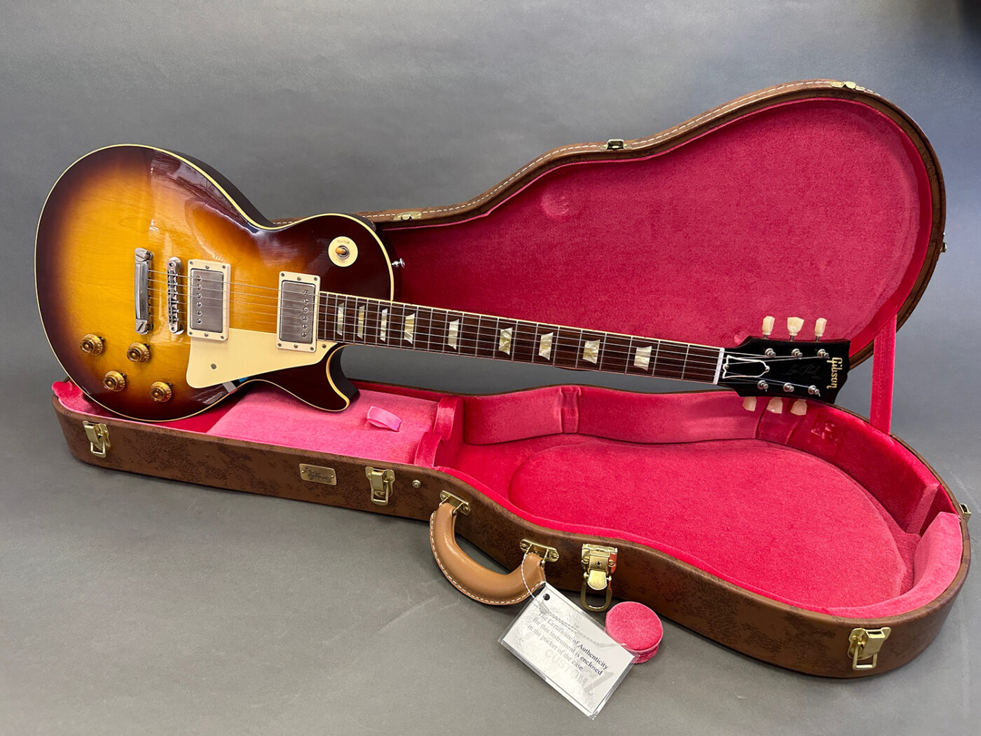Vintage Gibson Les Paul electric guitar with sunburst finish in brown hard shell case with pink plush interior and certificate of authenticity badge