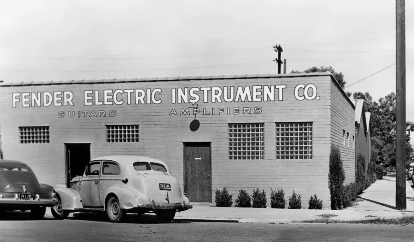 Vintage black and white photo of Fender Electric Instrument Co. building with cars parked in front.